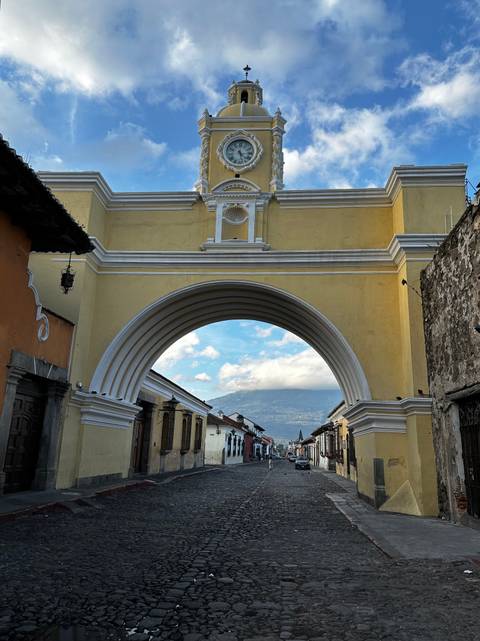       Iconic yellow Santa Catalina Arch frames a distant volcano above Antigua's colonial street.
  