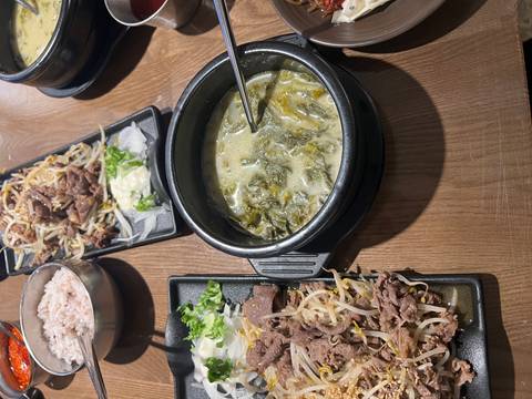       Traditional Korean meal featuring soup, grilled beef, bean sprouts and rice on a wooden table.
  