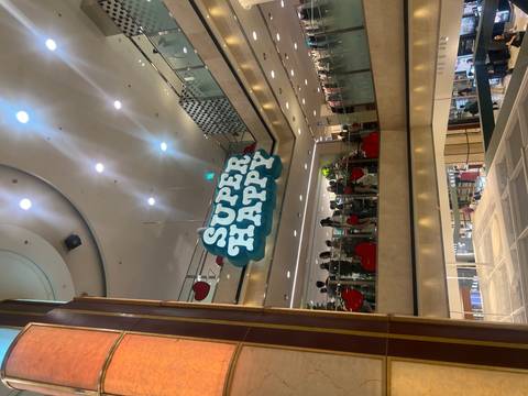       Interior of a shopping mall with a large ‘SUPER HAPPY’ sign hanging above crowds on multiple levels.
  