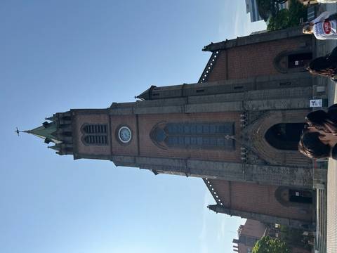       Gothic-style church tower rising into a clear sky with visitors gathered at its entrance.
  