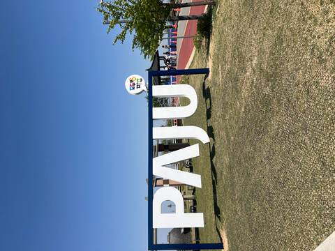       Outdoor sign spelling PAJU in a grassy park area under a clear sky with visitors nearby.
  