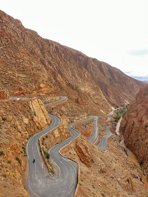       Serpentine mountain road cuts through steep, rugged canyon walls with cars navigating sharp switchbacks.
  