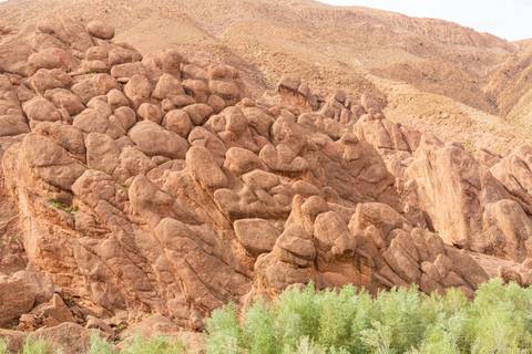       Rocky formations of reddish stone resembling stacks of rounded boulders rise against a desert hillside.
  