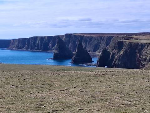       Dramatic sea stacks and sheer cliffs frame a vivid blue bay along Scotland’s rugged northern coast.
  