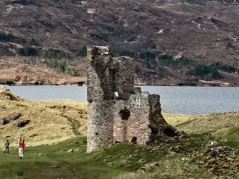       Ruined stone tower sits beside a loch amid rolling heather-clad hills in the Scottish Highlands.
  