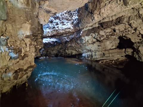      Dimly lit cave pool sparkles with reflections beneath rugged limestone walls.
  