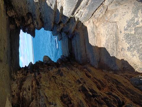       Stone window opening in cliff ruins frames a view of the blue sea below.
  