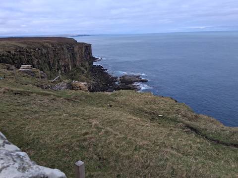       High moorland cliffs meet the vast grey waters of the North Atlantic under an overcast sky.
  
