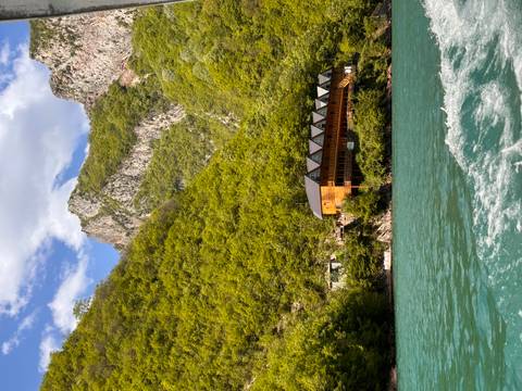       Wooden lodge on turquoise lake surrounded by steep green canyon walls and rugged peaks.
  