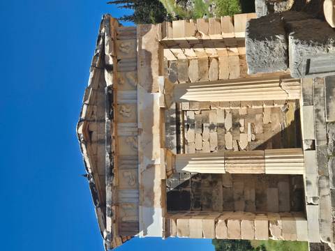       Classic stone treasury building with Doric columns and sculpted frieze set against a vivid blue sky.
  