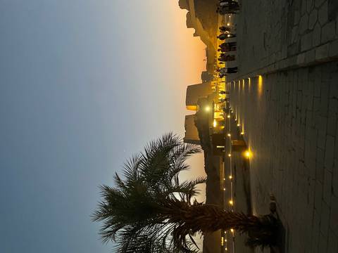       A palm-lined walkway lit by soft ground lights leads toward Luxor Temple at twilight.
  