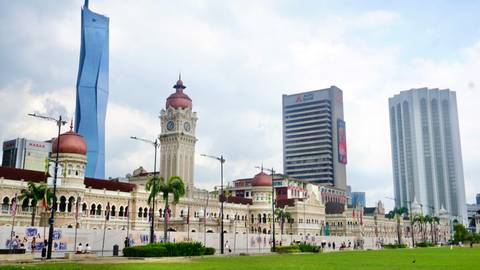      Kuala Lumpur’s Sultan Abdul Samad Building and modern skyscrapers rise behind a green field.
  