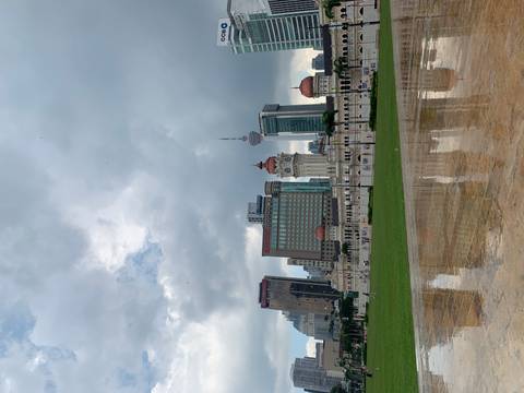       Historic colonial buildings and KL Tower stand beneath dramatic gray clouds and wet pavement reflections.
  