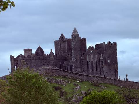      Medieval limestone Rock of Cashel castle rises atop a green hill under moody skies.
  