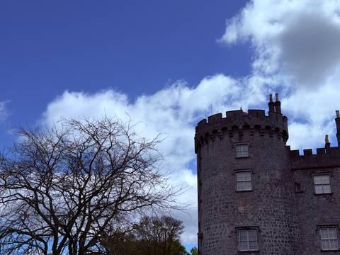       Stone turret of Kilkenny Castle framed against blue sky with bare tree branches.
  