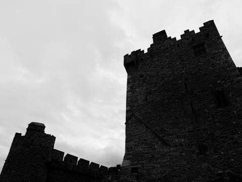       Moody black-and-white silhouette of a medieval stone tower against cloudy sky.
  