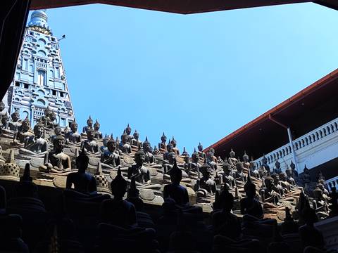       Silhouetted rows of seated Buddha statues rising toward a clear blue sky in a city temple courtyard.
  