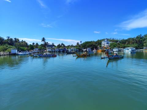       Calm harbour with colourful fishing boats reflected in turquoise water under a bright sky.
  