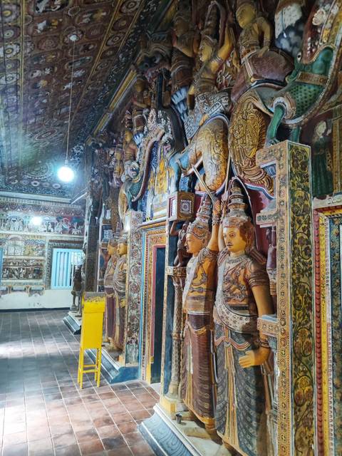       Elaborate temple corridor lined with painted wooden statues and intricate wall art.
  