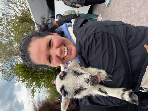       Smiling traveler cuddling a young lamb during a farm visit.
  