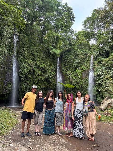       Group of travelers posing between twin jungle waterfalls surrounded by lush greenery
  