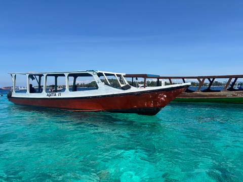       Wooden island taxi boat floating on crystal-clear turquoise waters with distant shoreline
  