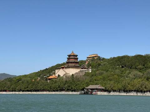       The Tower of Buddhist Incense rises above lush trees on Longevity Hill, reflected in the still waters of Kunming Lake beneath a cloudless blue sky.
  