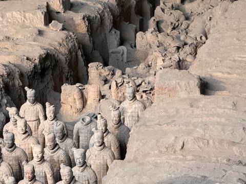       Excavation pit packed with life-sized Terracotta Warriors, some headless and partially unearthed, showcasing intricate armor details in muted clay tones.
  