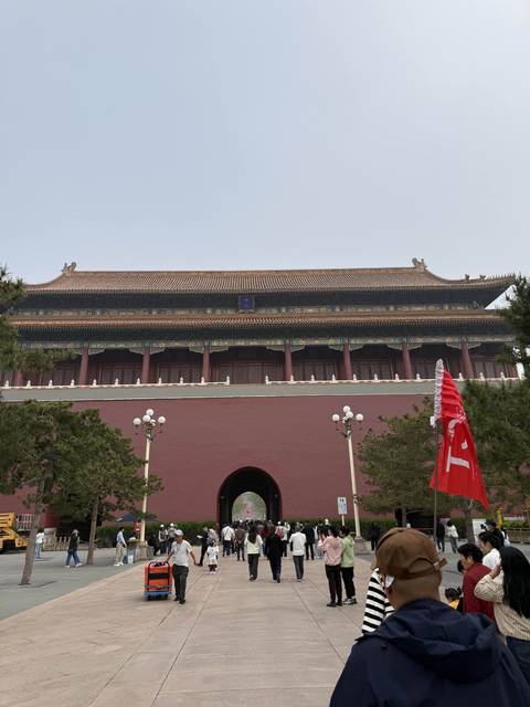       A grand hall of the Forbidden City with red columns, ornate eaves and a plain foreground wall under an overcast sky.
  
