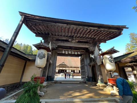       Traditional wooden entrance gate of a Japanese temple complex with visitors walking inside.
  