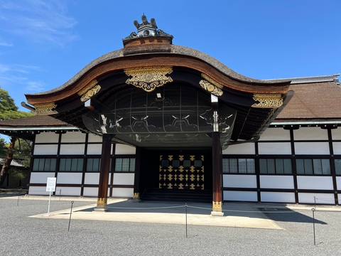       Elegant black-and-white wooden hall with ornate gilded roof details at Kyoto Imperial Palace.
  