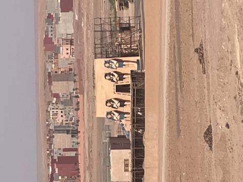       Distant view of an unfinished movie set with large Egyptian female statues in a desert edge town.
  