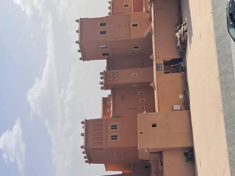       Adobe towers of a kasbah with a couple of locals near the entrance on a hazy afternoon.
  