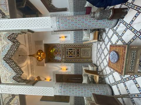       Opulent Moroccan riad interior with mosaic pillars, stained-glass door and patterned floor.
  