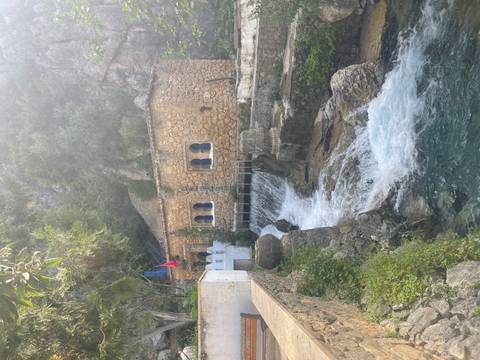       Small stone building beside a cascading stream in a lush, rocky mountain setting with a Moroccan flag.
  