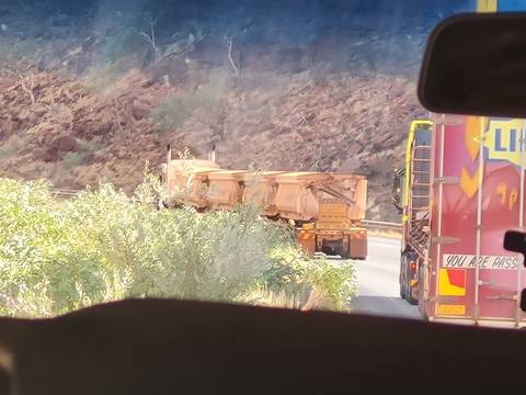       View through a vehicle windshield of large mining trucks on a dusty outback road.
  