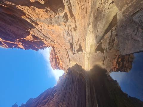      A narrow red-rock gorge with still water reflecting towering sandstone walls under a clear blue sky.
  