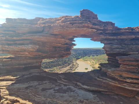       A natural sandstone window frames a river winding through a green gorge below.
  