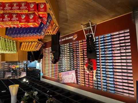       Interior of a Cailler chocolate shop with colourful chocolate bars stacked wall-to-wall and staff stocking shelves.
  