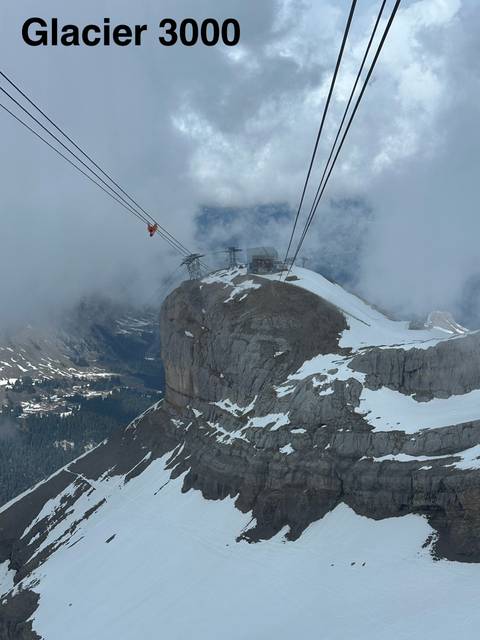       A snowy alpine peak with cable cars ascending through mist to a mountaintop station.
  