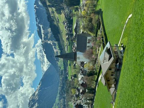      Picturesque alpine valley with a tall church steeple and snow-dusted peaks beyond.
  