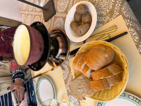       Table setting with a bubbling cheese fondue pot, sliced bread and boiled potatoes ready for dipping.
  