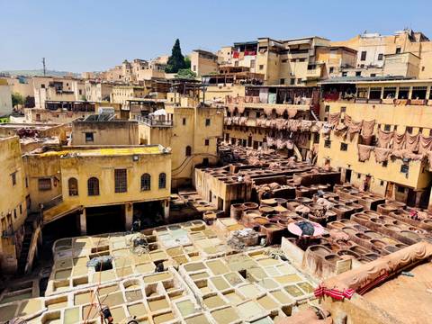       Elevated view of the Chouara leather tannery in Fes with rows of stone vats filled with dyes and hides drying on surrounding rooftops.
  