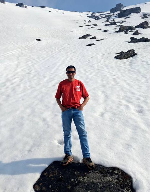       Smiling traveller in red shirt stands on a vast patch of untouched snow under bright light.
  