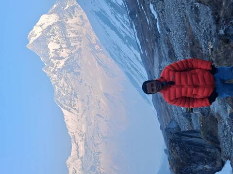       Traveller in bright orange jacket stands before snow-capped Himalayan peaks at dawn.
  