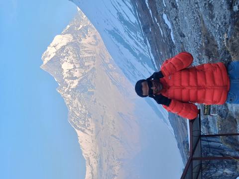      Hiker adjusting sunglasses while standing before a dramatic snow-capped Himalayan summit.
  