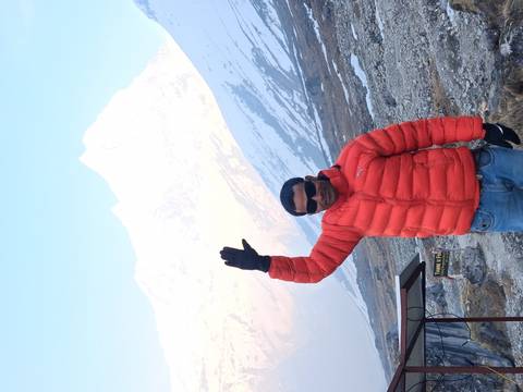       Man in sunglasses raising his hand with snow-white Himalayan peak behind him.
  
