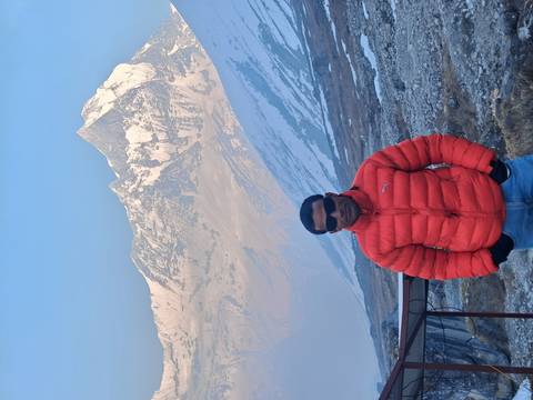       Portrait of a traveler in a puffy red coat set against the Himalayan range.
  