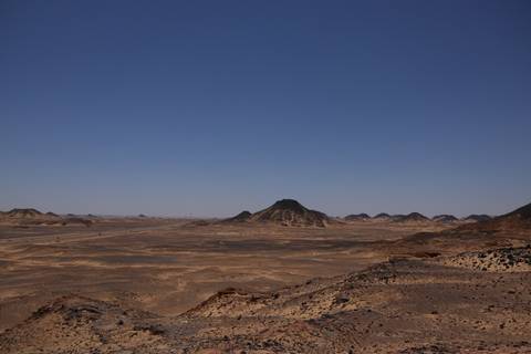       Expansive arid Black Desert landscape with isolated volcanic hill on horizon.
  
