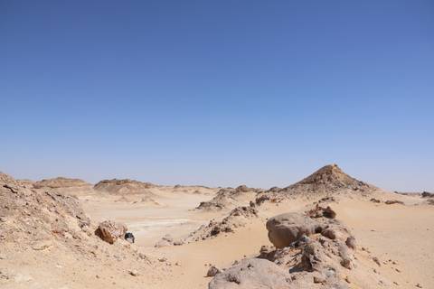       Rocky tan outcrops and sandy valleys under a cloudless blue Egyptian sky.
  